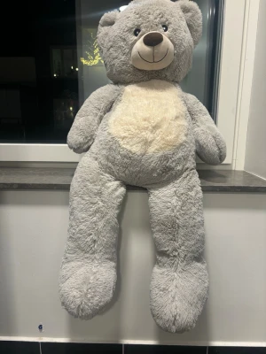 Stor grå nallebjörn plysch - Mysig och stor nallebjörn i mjuk grå plysch med ljusbeige mage och nos. Den har ett gulligt ansikte med broderade ögon och ett stort leende. Perfekt som dekoration eller kramkompis i soffan eller sängen.perfekt till alla hjärtans dag 