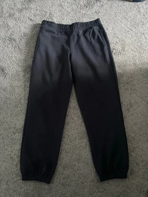 Svarta mjukisbyxor med resår - Säljer ett par svarta mjukisbyxor med resår i midjan och vid bensluten. Byxorna har en enkel och clean design utan synliga loggor och är tillverkade i mjukt material, perfekt för chill dagar. Bakficka finns på ena sidan.