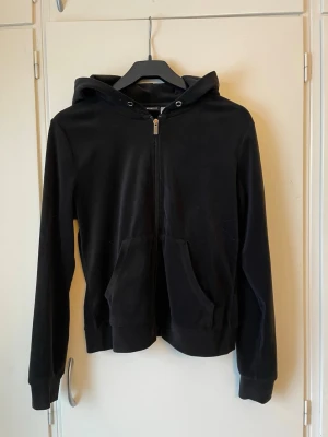 Svart zip hoodie med fickor - En klassisk svart hoodie med dragkedja framtill och två stora fickor. Hoodien har huva med snörning och ribbade muddar vid ärmslut och nederkant. Skönt mateial 