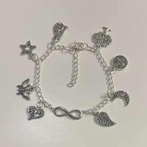 Silverfärgat armband med berlocker  - HANDGJORT Charmigt armband i silverfärg med flera olika berlocker. Kedjan är tunn och justerbar, perfekt för att ge en personlig touch till din stil.