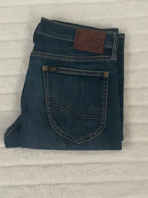 Mörkblå jeans från Lee - Snygga mörkblå jeans från Lee med klassisk femficksdesign och brunt läderpatch bak i midjan. Jeansen har raka ben och guldfärgade sömmar som ger en tidlös look. Perfekta till vardags och passar till det mesta. Tillverkade i mjukt denimtyg.