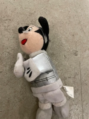 Musse Pigg mjukisdjur i rymddräkt - Säljer ett gulligt Musse Pigg mjukisdjur klädd i en silverfärgad rymddräkt. Dockan är svart, vit och beige med röda detaljer på munnen. Tillverkad i mjukt tyg och har broderade detaljer på ansiktet och dräkten. Perfekt för samlare eller som dekoration.