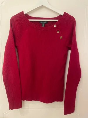 Röd stickad tröja - Stickad tröja från Ralph Lauren med knappar som är en cool detalj!  Storlek L men kan vara lite liten i storleken (44cm axelbredd och 61cm längd)  Väldigt bra skick men lite slitning av färgen på knapparna (se bild 5) Obs! katt finns i hemmet🩷