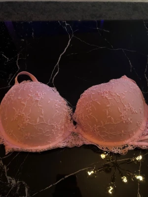 Ljusrosa push-up bh med spets - Söt ljusrosa push-up bh med vadderade kupor och vacker spets med blommönster. Dekorerad med en liten rosett och en glittrig detalj mellan kuporna. Axelbanden är justerbara och bh:n har fina spetskanter. Perfekt för dig som gillar romantiska detaljer. Passar C-D kupa 