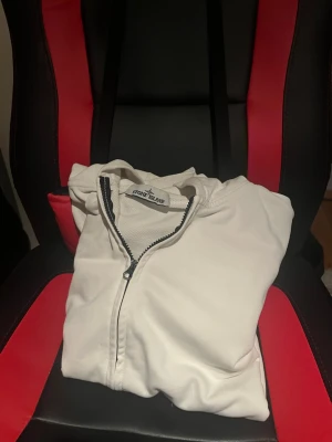 Vit hoodie med dragkedja Stone Island - Säljer en vit hoodie från Stone Island med dragkedja framtill och stor huva. Hoodien har en klassisk känguruficka och är tillverkad i mjukt material som känns skönt mot huden. Perfekt för dig som gillar stilrena och enkla plagg.