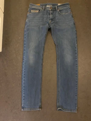 Blå raka jeans från Diesel - Säljer ett par klassiska blå jeans från Diesel med raka ben och snygga kontrastsömmar. Jeansen har fem fickor och en diskret logga på fickan fram. Perfekta till en avslappnad stil och tillverkade i slitstarkt denimtyg.. Dom är använda då.de va sonens favorit jeans innan han växte ur dom. Men hela och rena 