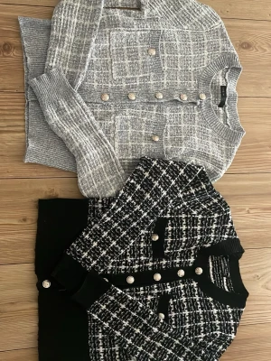 Två tweedkoftor med dekorativa knappar - Säljer två trendiga tweedkoftor från SHEIN. Ena är grå med vita detaljer och dekorativa guldknappar, den andra är svartvit med samma typ av knappar. Båda har rund hals, fickor framtill och ribbade muddar. Perfekta för en chic och stilren look.