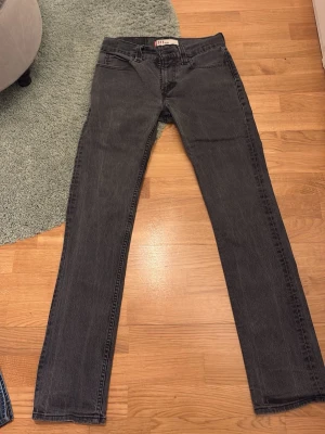 Svarta/grå Levi's 511 slim jeans - Säljer ett par svarta Levi's 511 slim jeans med klassisk femficksdesign och rakt ben. Jeansen har en snygg tvättad finish och är tillverkade i bomull med lite stretch för extra komfort. Perfekta för en avslappnad och stilren look. Hör av er vid frågor.👍