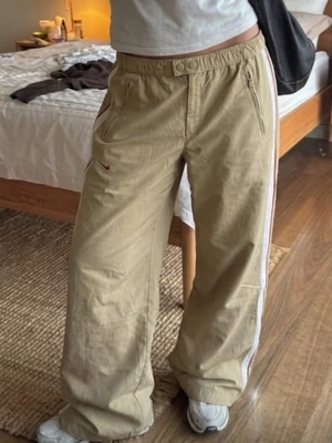 Vintage Nike byxor  - Säljer dessa sjukt snygga vintage Nike byxor i beige med randiga detaljer på sidan! Low waist med elastisk midja och baggy fit. I mycket bra skick. Hör av er vid frågor ❤️🌸