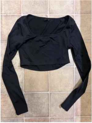 Svart croppad långärmad topp - Snygg svart croppad topp med långa ärmar och rundad urringning. Perfekt att matcha med höga jeans eller kjol för en trendig look. Tunn och stretchig kvalitet som sitter skönt på kroppen.