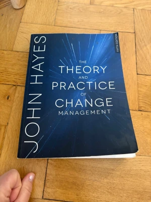 The Theory and Practice of Change Management - Kursbok på engelska: 'The Theory and Practice of Change Management' av John Hayes, femte upplagan. Omslaget är mörkblått med vita bokstäver och ett abstrakt ljusmönster. Perfekt för dig som pluggar management eller organisation.