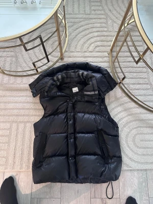  Burberry jacka   - Snygg svart dunväst från H&M med avtagbar huva och dragkedja framtill. Västen har två praktiska fickor med dragkedja och quiltad design. Perfekt för lager-på-lager och håller dig varm under kyliga dagar den passar L också 