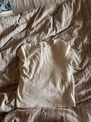 Vit basic t-shirt från H&M - En enkel vit t-shirt från H&M med rund hals och korta ärmar. Tillverkad i mjuk bomull som känns skön mot huden. Perfekt att matcha med jeans eller kjol för en clean och stilren look.