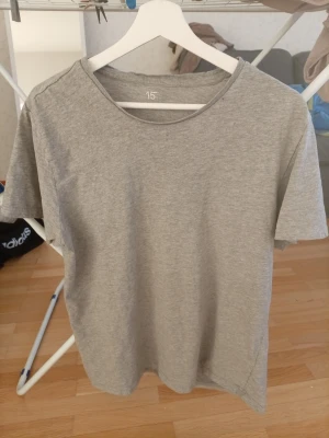 Grå basic t-shirt från Lager 157 - Enkel och stilren grå t-shirt från Lager 157 . T-shirten är kortärmad och har en klassisk rund halsringning. Tillverkad i mjuk bomull, perfekt för en avslappnad och clean look. Står int storlek men teo de ä XL. Ser ut som de står lite kvar av de