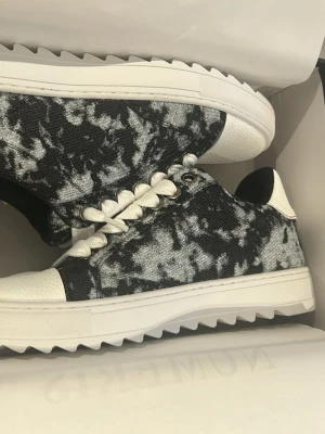 Svarta och vita sneakers från Numeris - Snygga sneakers från Numeris med svart och vit batikmönstrad canvas, vita detaljer och grov sula. Skorna har vita skosnören och en låg profil som ger en modern vibe. Perfekta för dig som gillar att sticka ut med din stil.