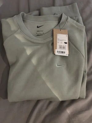 Ljusgrön Nike Dri-FIT sweatshirt - Helt ny, aldrig använd, Ljusgrön sweatshirt från Nike med Dri-FIT material som håller dig torr och bekväm. Tröjan har rund halsringning, diskret Nike-logga på bröstet och ribbade muddar vid ärmslut och nederkant. Perfekt för en avslappnad och sportig look.