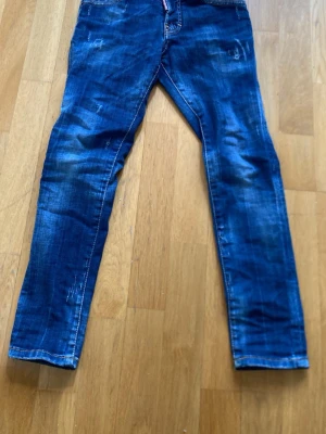 Blå slim fit dsq2 jeans - Säljer ett par blå slim fit jeans med coola slitningar och tvättade detaljer. Jeansen har klassisk femficksdesign och är tillverkade i denim. Perfekt för dig som gillar en avslappnad och trendig look.
