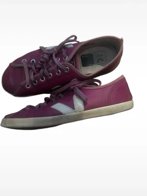 Rosa Veja sneakers med vit detalj - Snygga rosa sneakers från Veja med vit V-logga på sidan och vita sulor. Skorna har lågt skaft, klassisk snörning och är tillverkade i läder och textil. Perfekta för dig som gillar stilrena och trendiga sneakers med en färgklick.