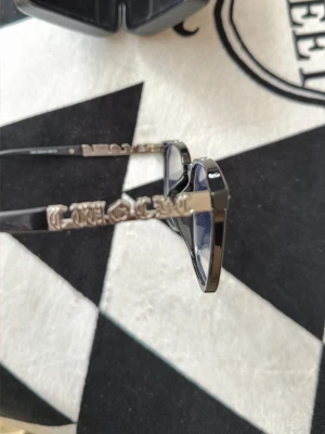Svarta solglasögon från chorme hearts - Snygga svarta solglasögon från chrome hearts med fyrkantiga bågar och silverfärgade detaljer på skalmarna. Klassisk och trendig design som lyfter vilken outfit som helst. Perfekta för dig som vill sticka ut med en exklusiv accessoar.