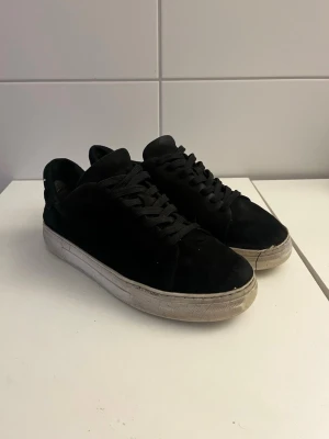Svarta selected home i mocka  - Stilrena svarta sneakers i mocka med klassisk vit gummisula och svarta skosnören. Låg modell som passar perfekt till jeans eller streetwear. Enkel och clean design utan synliga loggor, vilket gör dem lätta att matcha med olika outfits.