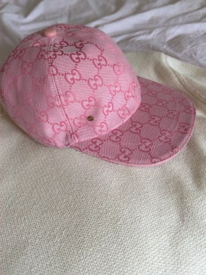 Rosa  keps med mönster - Säljer en rosa keps  med ikoniskt GG-monogram i hela tyget. Kepsen har böjd skärm och är tillverkad i ett slitstarkt tyg med vit insida. Perfekt för dig som vill ha en trendig accessoar med lyxig känsla.
