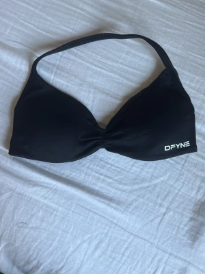 Impact Strappy Bra från DFYNE - Säljer en svart sport-bh från DFYNE med enkel design och smala axelband. Bh:n har lätt vaddering och logga i vitt på ena sidan. Perfekt för träning eller chill dagar. Materialet känns mjukt och stretchigt. Är lite tajt så passar till xs och har aldrig använt 