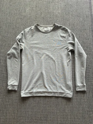 Ljusgrå stickad långärmad tröja - En stilren ljusgrå sweatshirt med rund hals och långa ärmar. Tröjan har en enkel design utan tryck eller mönster och är tillverkad i mjukt bomullsmaterial. Perfekt för en avslappnad och clean look.