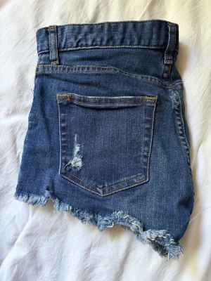 Blå jeansshorts med fransig kant - Pris kan diskuteras Säljer ett par blå jeansshorts med fransig kant och slitna detaljer. Shortsen har klassiska fickor både fram och bak samt synliga sömmar i kontrastfärg. Perfekta för en avslappnad och trendig look. Sjukt snygga för sommaren. Köpta i Polen 