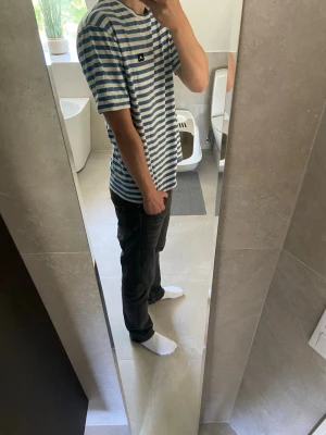 Randig blåvit t-shirt från J-lindeberg - Säljer en stilren blåvit randig t-shirt från J-lindeberg T-shirten har korta ärmar, klassisk passform och är tillverkad i mjuk bomull. Perfekt för dig som gillar enkel men snygg stil. Liten logga på bröstet för en clean look.  Var inte rädd att höra av dig vid funderingar