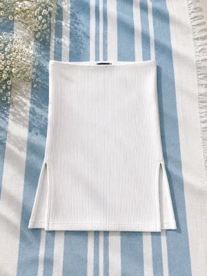 Vit ribbad bandeau topp - 🤍 Vit ribbad bandeau-topp med diskreta slitsar vid sidorna ✨ Superfin basic som ändå sticker ut lite extra 🫶🏻 Stretchigt och lite grövre ribbat material som sitter snyggt på. Enkel att matcha till jeans, kjol eller shorts för en clean och trendig look 🤍 Använd få gånger och i fint skick! 🦋Står strl L men passar bättre som s