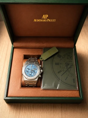 Audemars Piguet Royal Oak blå klocka - Exklusiv Audemars Piguet Royal Oak herrklocka i rostfritt stål med ikonisk åttakantig boett och blå urtavla med struktur. Klockan har kronograf, datumvisning och länkarmband i metall. Levereras i originalbox med certifikat.