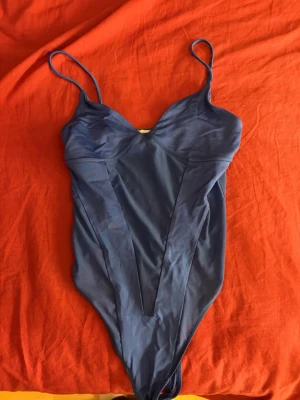 Mörkblå body med tunna axelband - Snygg mörkblå body med tunna axelband och v-ringad urringning. Modellen har en smickrande skärning framtill och är tillverkad i ett glansigt, stretchigt material som känns mjukt mot huden. Perfekt för dig som vill ha en enkel men stilren look.  Från bershka 
