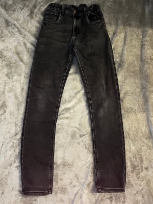 Svarta slimfit  jeans  - Säljer ett par svarta slimfit jeans med klassiska fem fickor. Jeansen har stretchig passform och smala ben, perfekta till sneakers eller boots. Materialet är mjukt denim med lätt tvättad look och knappgylf framtill. Vid frågor hör av dig och priset kan alltid diskuteras 