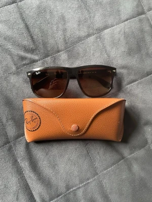 Ray-Ban Boyfriends  - Snygga svarta Ray-Ban Boyfriens solglasögon med klassisk form och mörka glas. Kommer med ett brunt Ray-Ban fodral i skinnimitation. Perfekta för soliga dagar och ger en cool vibe till din outfit.