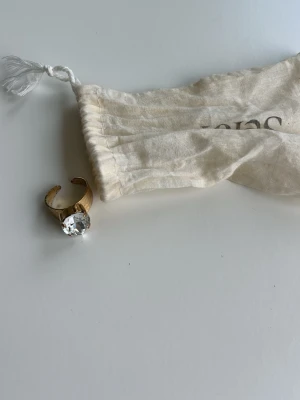 Guldfärgad ring med stor sten - Snygg guldfärgad ring med en stor, klar sten framtill. Ringen har öppen baksida vilket gör den justerbar i storlek. Perfekt statement-piece för dig som gillar att sticka ut med dina accessoarer.