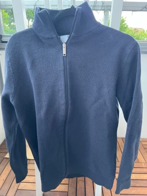 Marinblå ziptröja från Selected Homme - Snygg marinblå ziptröja från Selected Homme med hög krage och diskret strukturstickning. Tröjan har dragkedja framtill och ribbade muddar vid ärmslut och nederkant. Perfekt för lager på lager och enkel att matcha med olika outfits.
