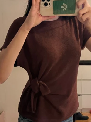 Zara Vinröd topp med knyt i midjan - Säljer en vinröd topp med korta ärmar och rund hals. Toppen har en snygg knytdetalj i midjan som ger en cool twist till outfiten. Perfekt att styla med jeans eller kjol för en trendig look. Från Zara, storlek S 