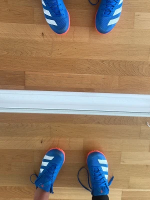 Adidas blåa spikskor med röd sula - Säljer ett par Adidas spikskor i blått med röd sula och metallspikar. Skorna har snörning och är designade för löpning på bana. Ovandelen är i meshmaterial för bra ventilation och lätt känsla. Perfekta för friidrottsträning och tävling.