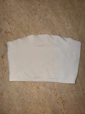 Vit bandeau tubtopp - Säljer en vit bandeau tubtopp i stretchigt och mjukt material. Toppen är helt axelbandslös och har en clean, minimalistisk look som är enkel att styla till olika outfits. Perfekt för sommaren och funkar lika bra till jeans som kjol.