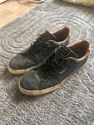 Mörkblå sneakers från Pepe Jeans - Säljer ett par mörkblå Pepe Jeans sneakers. Använda men fortfarande i helt ok skick. Sulan är lite trasiga som man ser på bild 3 och 4. Det är bara användning. Det finns mycket användning kvar. Perfekta som vardagsskor. Säljs eftersom de inte används längre.  Storlek: 43 Skick: 7/10 Pris kan diskuteras :)