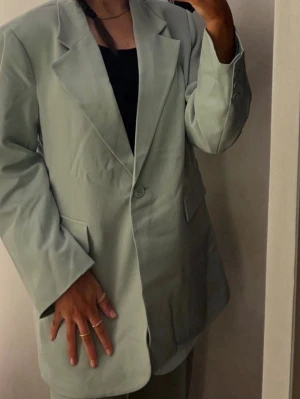 Ljusgrön oversized kavaj - Trendig ljusgrön oversized kavaj från Bik Bok med klassisk krage, en knapp framtill och två fickor med lock. Kavajen har långa ärmar och en rak passform som ger en cool och avslappnad look. Perfekt att styla med både jeans och kjol.