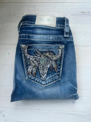Miss Me bootcut jeans med brodyr - Snygga blå bootcut jeans från Miss Me med slitningar och unik brodyr på bakfickan i form av en tjurskalle och fjädrar. Jeansen är i storlek 25 och längd 34. De är mid waist och är i bra skick😊
