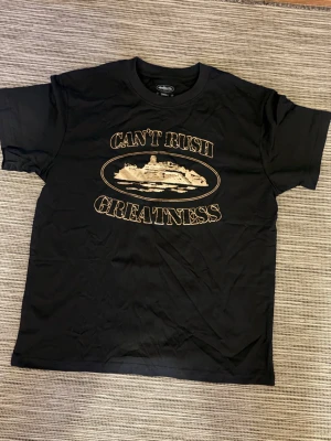 Svart t-shirt Can't Rush Greatness - Svart t-shirt med tryck av en yacht och texten 'CAN'T RUSH GREATNESS' på bröstet. Klassisk passform med rund hals och korta ärmar. Perfekt för dig som vill sticka ut med ett statement-plagg.