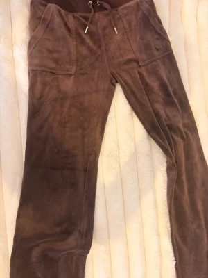 Bruna velourbyxor Juicy Couture S - Mysiga bruna mjukisbyxor från Juicy Couture i velourmaterial. Byxorna har bred resår i midjan med dragsko och stora fickor framtill. Perfekta för chill dagar och har den klassiska Juicy-looken som aldrig går ur tiden. Pris kan diskuteras 