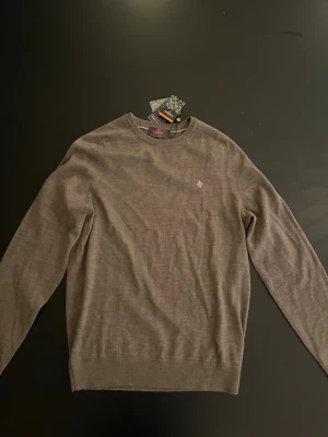 Morris sweatshirt - Snygg brun tunnstickad tröja med rund halsringning och diskret broderad logga på bröstet. Tröjan har långa ärmar och ribbade muddar vid ärmslut och nederkant. Perfekt för lager på lager och enkel att matcha med olika outfits.