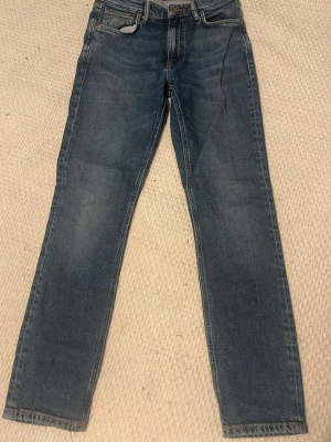Nudie jeans - Säljer ett par klassiska blå jeans ifrån nudie med rak passform och snygga broderade detaljer på bakfickorna. Lappen har gått av men nudie ger gratis lagningar, Jeansen har fem fickor, normal midja och är gjorda i slitstarkt denimtyg. Perfekta till vardagslooken!