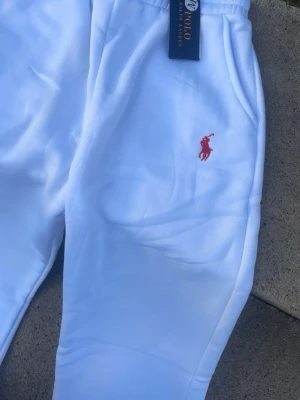 Vita mjukisbyxor från Polo Ralph Lauren - Snygga vita mjukisbyxor från Polo Ralph Lauren med klassisk röd broderad logga på benet. Byxorna har resår i midjan och är tillverkade i mjukt material som känns skönt mot huden. Perfekta för en avslappnad och stilren look.