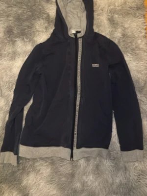 Mörkblå hoodie från Hugo Boss - Xs - Snygg mörkblå hoodie från Hugo Boss med dragkedja framtill och gråa detaljer på muddar, nederkant och insidan av huvan. Liten BOSS-logga på bröstet. Perfekt för en chill och stilren look. Kan sänka priset vid snabb affär 💨 