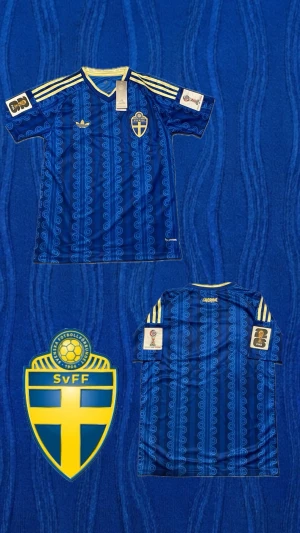 Äkta Sverige Vm Tröja + VM PATCH - Säljer en blå Sverige fotbollströja från Adidas med gula detaljer och tre ränder på axlarna. Tröjan har Sveriges landslagsemblem på bröstet och ett mönster i olika blå nyanser. Perfekt för dig som vill stötta landslaget med stil.