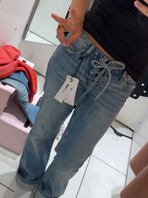 Helt nya jeans m snörning fram - Säljer ett par ljusblå jeans med unik snörning i midjan istället för vanlig knapp. Jeansen har raka ben och en avslappnad passform. Perfekta för dig som vill ha något lite annorlunda och trendigt i garderoben. Materialet är klassisk denim.